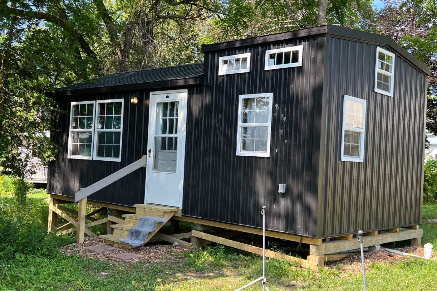 A sleek 14x28 cabin with a modern black metal exterior is nestled in a lush green setting.
