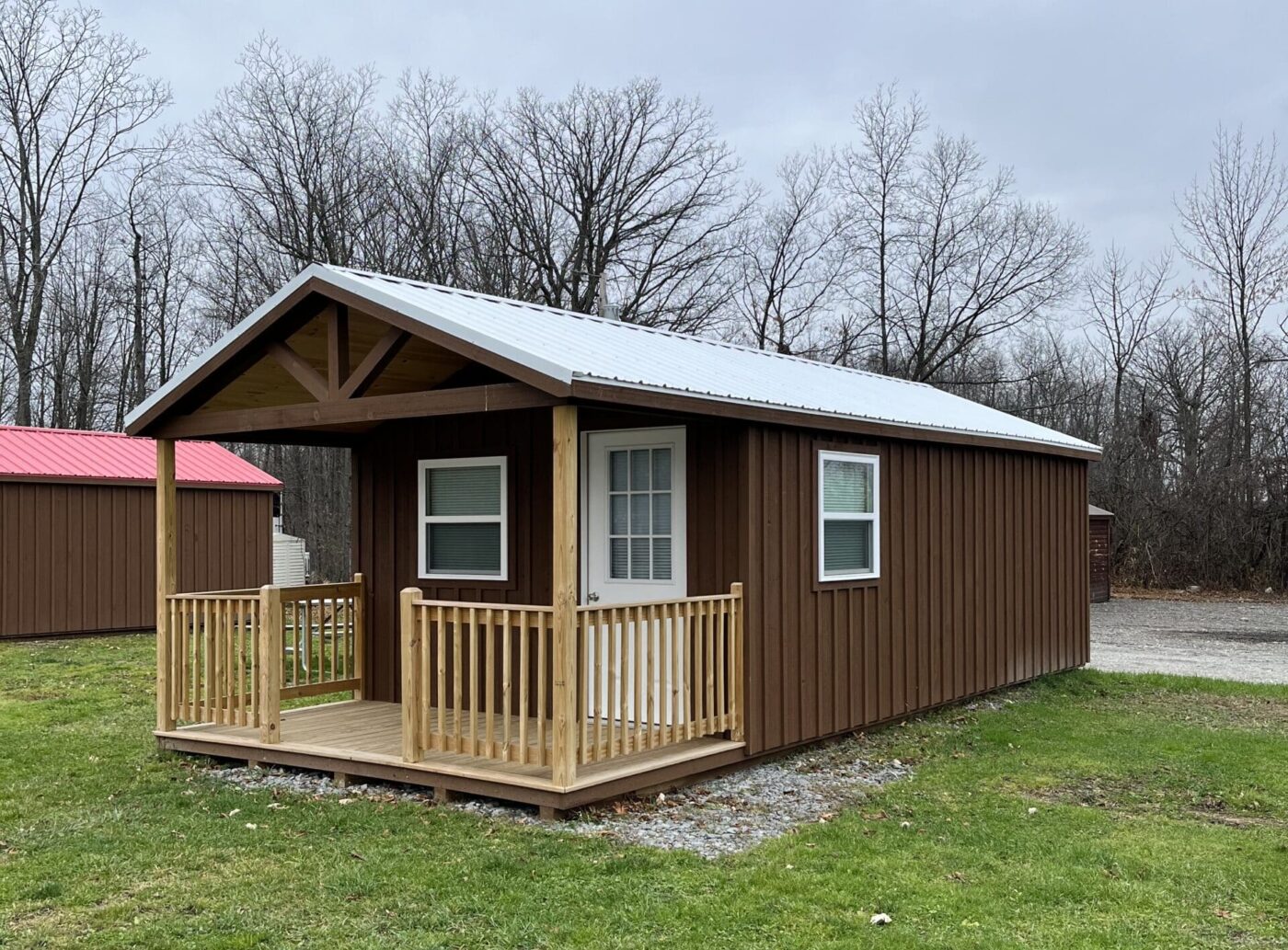 Brown cabin shed with white-trimmed windows - white door and roof in leafless trees - one of our many sheds near Cheektowaga