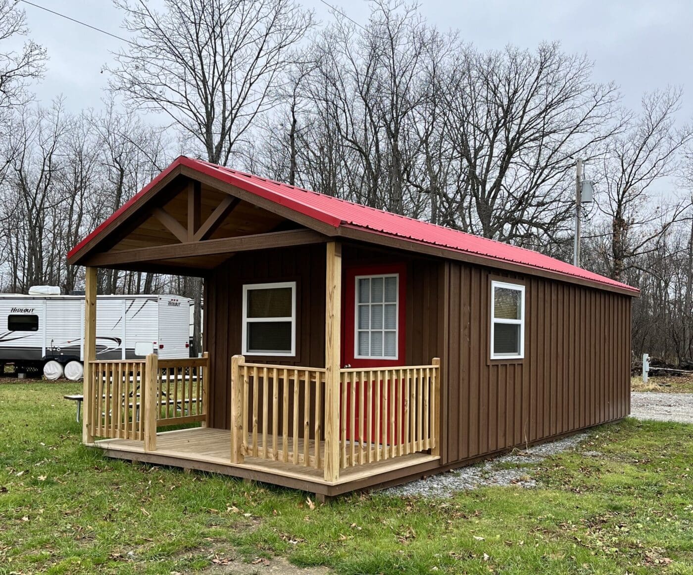 One of our cabin sheds near Mt Morris NY - brown with red door and white-framed windows, wooden porch and fence-red roof-leafless trees in background