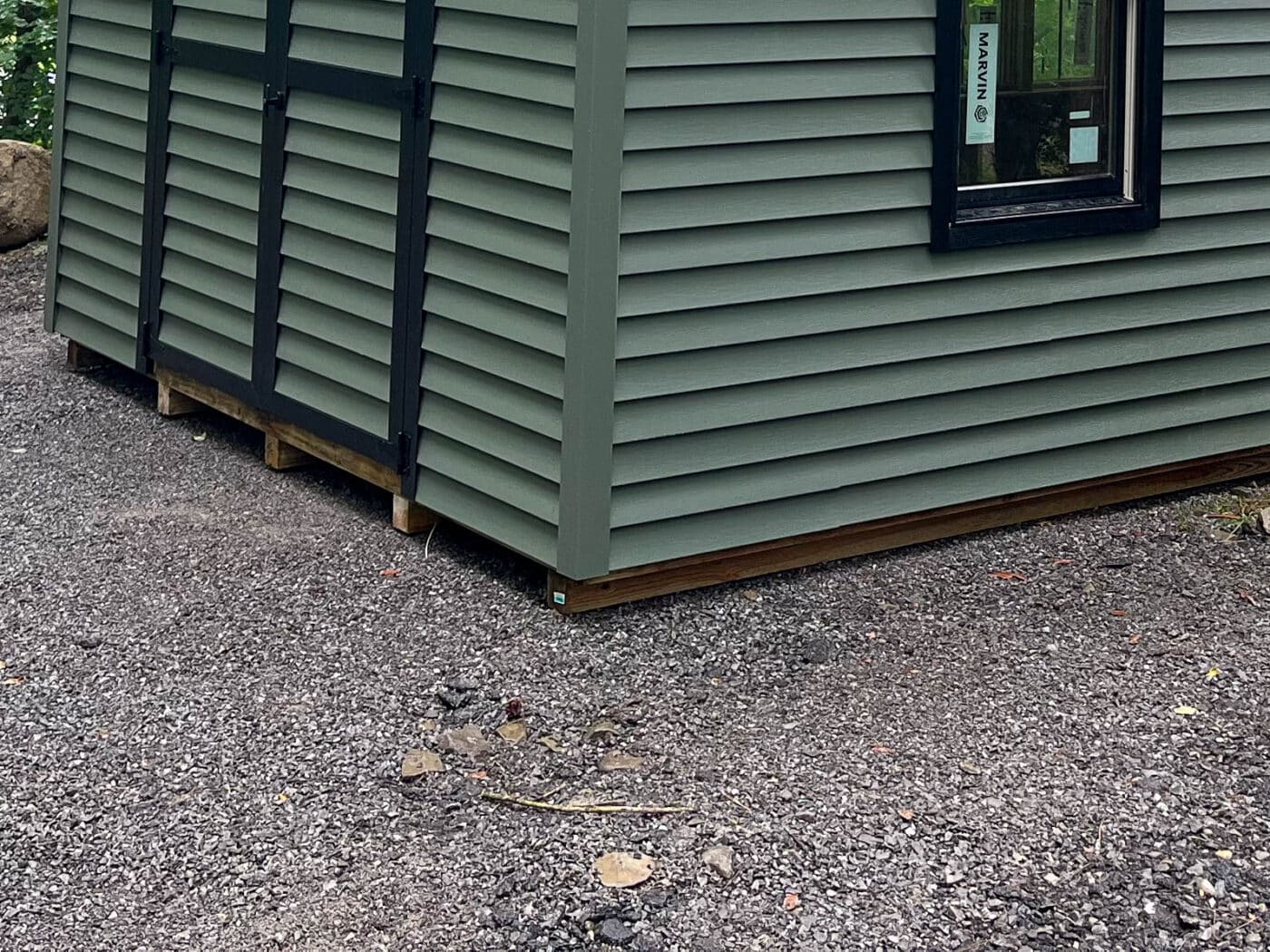 Porch Support Looks Solid, But Gravel Base is Uneven – The shed's porch and structure are well-supported, but the gravel base beneath the shed is uneven and not properly compacted. Extending the gravel base beyond the shed’s edges and leveling it would improve drainage and prevent settling over time.