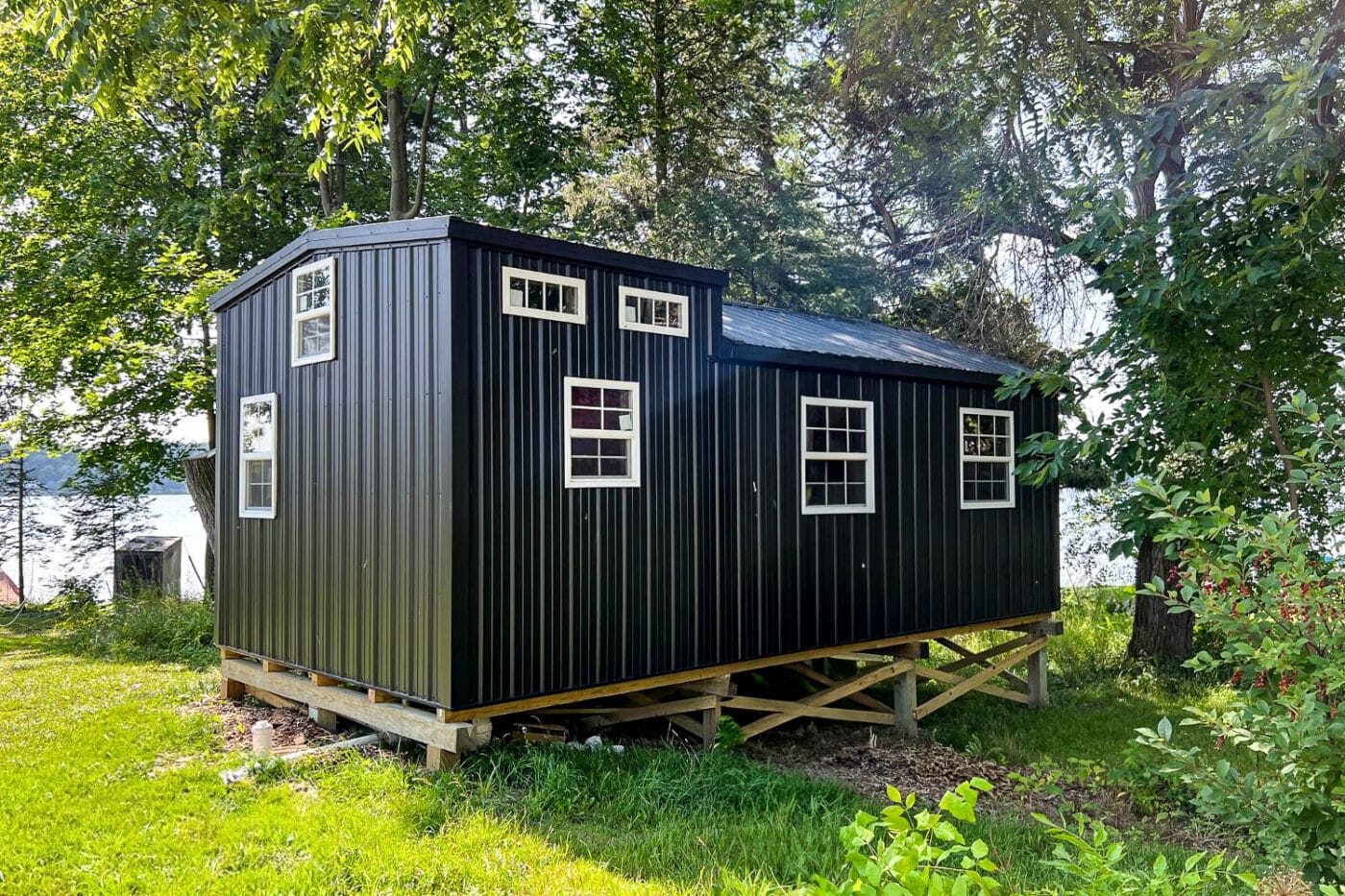 Modern black portable shed with multiple windows, elevated on a grassy clearing.