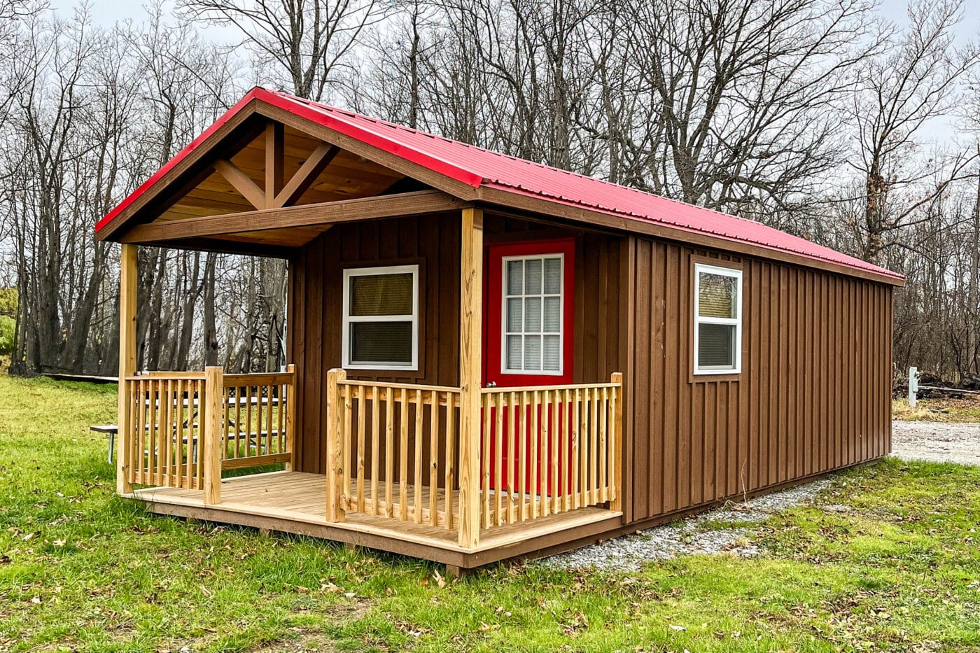 Custom cabin with a red metal roof, porch, and brown wooden siding surrounded by trees.